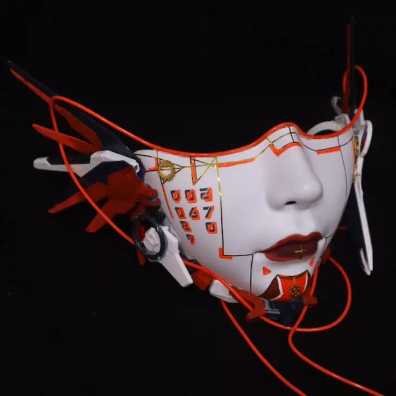 Może przedstawiać: Biała maska z geometrycznym wzorem i czerwonymi i złotymi akcentami. Maska ma stylizowaną twarz z czerwonymi ustami i klawiaturą numeryczną na czole.