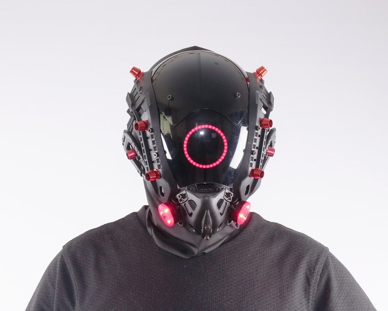 May include: A black helmet with red lights and a circular red light in the front. The helmet has a futuristic design.