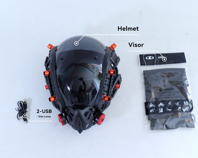 May include: A black motorcycle helmet with a clear visor and red accents. The helmet has a built-in face mask and two USB ports for side lamps. The helmet comes with a black carrying bag and a warning label.
