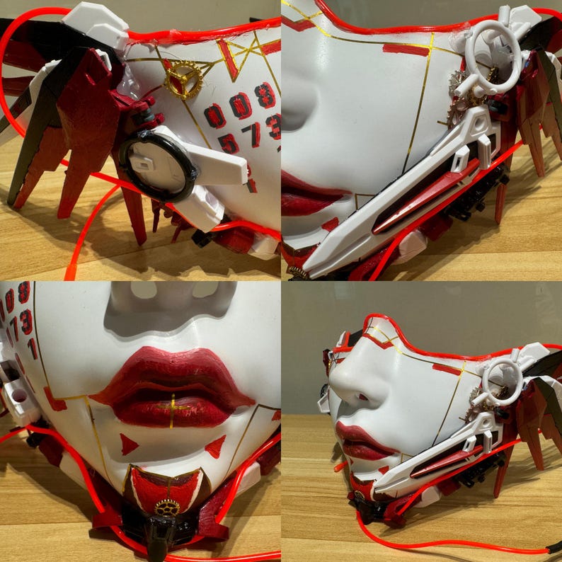 Może przedstawiać: Biała i czerwona maska ​​na twarz z misternymi detalami, w tym czerwono-białym skrzydłem, złotym zębatym kołem i czerwono-białym ostrzem. Maska ​​ma czerwone usta i białą twarz z czarnymi cyframi na czole. Maska ​​leży na drewnianej powierzchni.