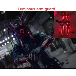 May include: A person wearing a black and red futuristic costume with glowing red arm guards. The arm guards are made of black plastic with red LED lights. The person is standing in front of a white wall. The text "Luminous arm guard" is written in red letters at the top of the image.