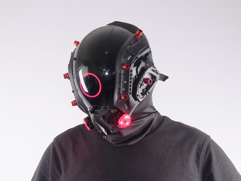 May include: A black helmet with red lights and a black face mask. The helmet has a circular red light on the front and several red lights on the sides.