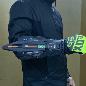 Puede incluir: Guante y protector de brazo de motocross negro y verde neón. El guante presenta el logotipo de Fox en verde neón y negro. El protector de brazo es negro con detalles en rojo y naranja y diseños geométricos. El protector de brazo tiene las letras "GK".