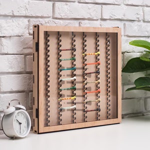 May include: A wooden display case with a glass front, showcasing a collection of colorful golf tees. The case has a decorative, laser-cut design around the edges.