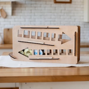 May include: Wooden organizer with a slanted shelf and compartments for storing canned goods. The organizer is made of light brown wood and has a black arrow pointing to the right.
