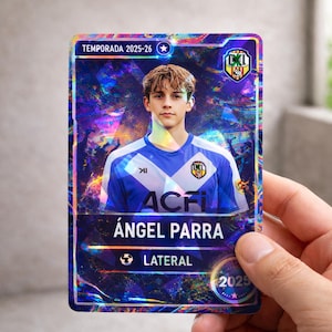 Puede incluir: Una tarjeta coleccionable de fútbol con diseño holográfico. Muestra a un joven con camiseta azul y blanca. El texto "TEMPORADA 2025-26" y el nombre "ÁNGEL PARRA" con "LATERAL" están presentes. La tarjeta es sostenida por una mano.