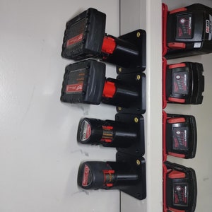 May include: A wall-mounted battery storage rack with six black battery holders and six red and black batteries. The batteries are labeled "Milwaukee REDLITHIUM XC4.0".