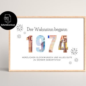 May include: A framed print with the year "1974" spelled out with currency, and the German text "Der Wahnsinn begann" above it. The print also includes the text "HERZLICHEN GLÜCKWUNSCH UND ALLES GUTE ZU DEINEM GEBURTSTAG!" and decorative starbursts.