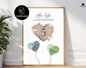 May include: A framed print with the text "Alles Liebe zu eurer Holzhochzeit" and a wooden heart with the number 5. Two heart-shaped balloons made of currency are below the heart. The print has a gold frame.