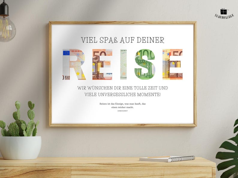 Geldgeschenk Reisekasse in einem Holzbilderrahmen hängt an einer beigen Wand über einem Sideboard. Daneben hängt eine Lampe und auf dem Sideboard steht ein Kaktus und liegt ein Notizbuch. Neben dem Sideboard steht eine weitere Pflanze.