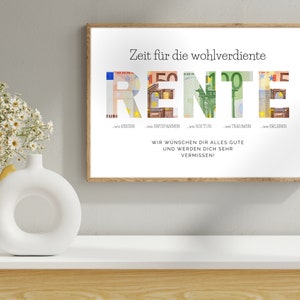 Geldgeschenk zur Rente in einem Holzbilderrahmen an einer grauen Wand über einem Sideboard mit Blumen und Deko darauf