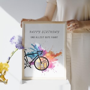 Eine Frau vor einer weißen Wand hält ein Geldgeschenk Fahrrad Geburtstag in einem Holzbilderrahmen. An dem Geschenk lehnt eine lila-gelbe Blume.