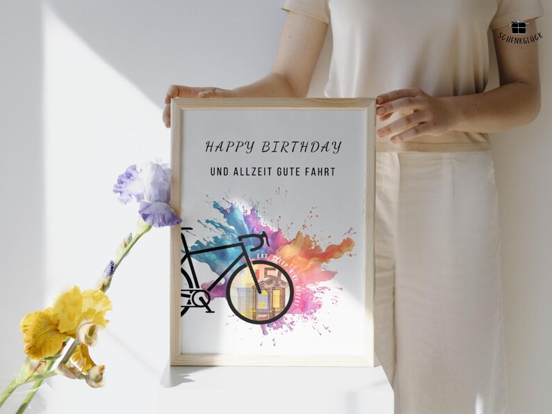 Eine Frau vor einer weißen Wand hält ein Geldgeschenk Fahrrad Geburtstag in einem Holzbilderrahmen. An dem Geschenk lehnt eine lila-gelbe Blume.