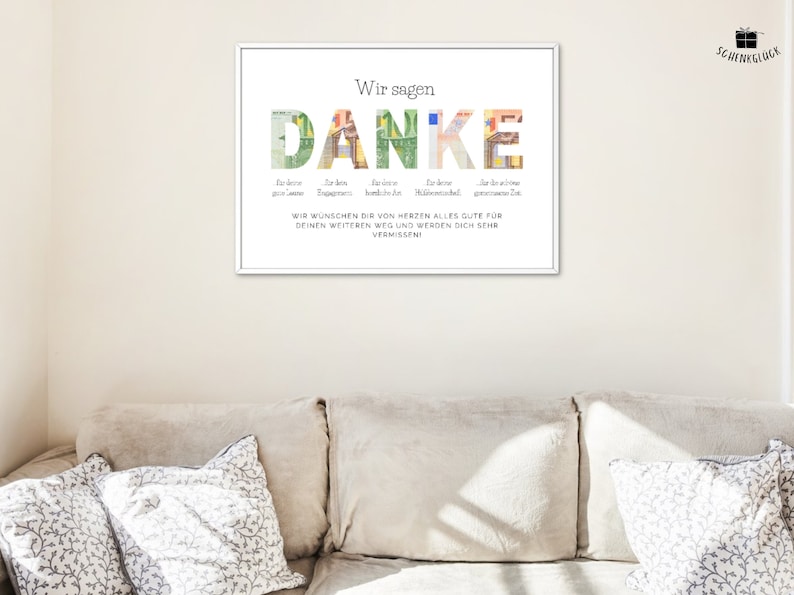 Abschiedsgeschenk Kollegin in einem weißen Bilderrahmen an einer beigen Wand über einem Sofa mit Kissen