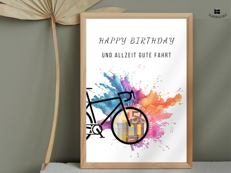 Geldgeschenk Fahrrad Geburtstag in einem Holzbilderrahmen vor einer grünen Wand neben einem getrockneten Palmenblatt