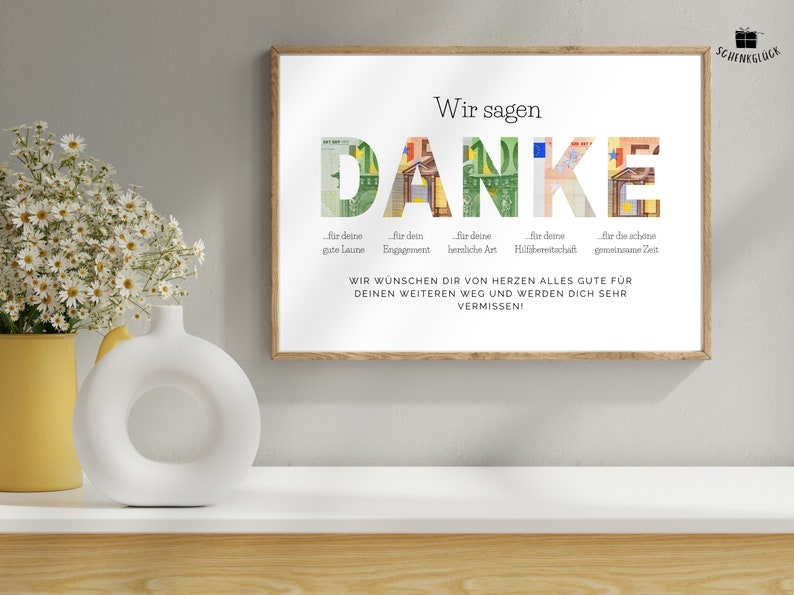 Abschiedsgeschenk Kollegin in einem Holzbilderrahmen über einem Regal mit einer Vase und einer Blume darauf