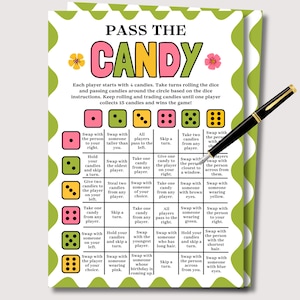 May include: A colorful game card titled "PASS THE CANDY" with instructions and dice illustrations. The card features a green and white border with floral accents and a black pen resting on the right side.