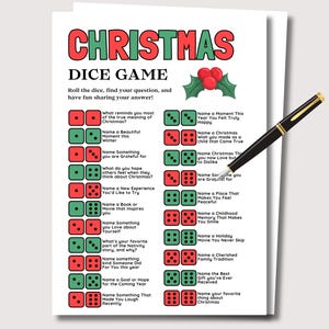 May include: A white card featuring a Christmas dice game with red and green text. The game prompts players to answer questions based on dice rolls. A black pen with gold accents lies on the card.