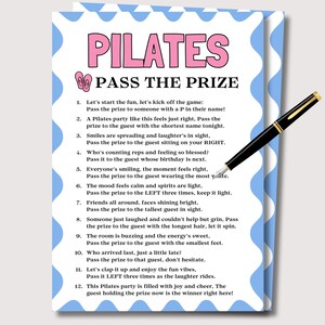 May include: A Pilates party game card with a blue and white wavy border. The words "PILATES PASS THE PRIZE" are in pink and black. A black pen with gold accents rests on the card, ready to be used.