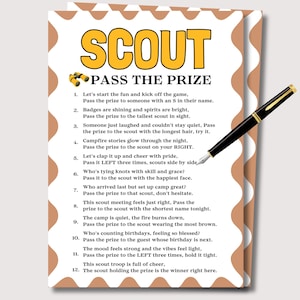 May include: A white card with a brown border and the words "SCOUT PASS THE PRIZE" in yellow and black. A black and gold pen rests on the card. The card contains a list of instructions for a game.