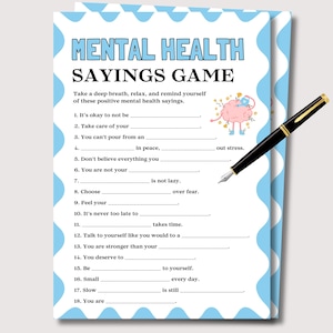 Puede incluir: Una tarjeta del juego "Mental Health Sayings" con un borde azul y blanco, con indicaciones para completar frases sobre salud mental positiva. Un bolígrafo negro con detalles dorados descansa sobre la tarjeta. La tarjeta incluye texto como "It's okay to not be".