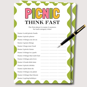May include: A white game sheet with green and white wavy borders, featuring the text "PICNIC THINK FAST" in pink, yellow, and black. The sheet includes prompts to list picnic-related items. A black and gold pen rests on the sheet.