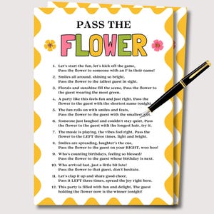 May include: A party game card with the text "PASS THE FLOWER" in colorful letters. The card has a yellow and white border with flower illustrations. A black and gold pen rests on the card, ready to play.