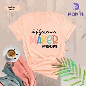 May include: A peach colored t-shirt with the text "difference maker #principal" in colorful letters.