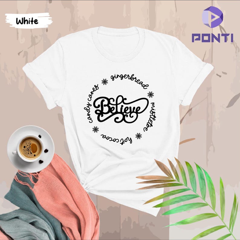 May include: White t-shirt with a black circle design that says "Believe" in a festive font. The circle is surrounded by snowflakes and the words "gingerbread", "mistletoe", "joy of season", and "candy canes".