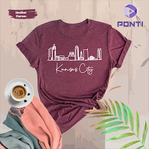 May include: Heather maroon t-shirt with a white outline of the Kansas City skyline and the text "Kansas City".