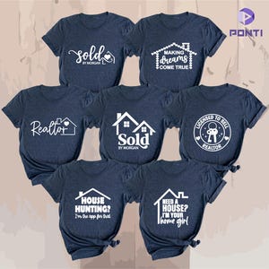 May include: A selection of navy blue t-shirts featuring white graphic designs and text. The designs include phrases such as "Sold," "Making Dreams Come True," and "Realtor," accompanied by house illustrations. These shirts are likely aimed at real estate professionals.