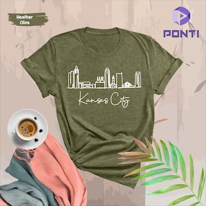 May include: A heather olive t-shirt with a white outline of the Kansas City skyline and the text "Kansas City".