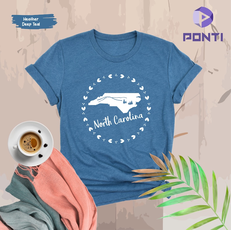 May include: A heather deep teal t-shirt with a white outline of the state of North Carolina and the words "North Carolina" inside a circle of white hearts.