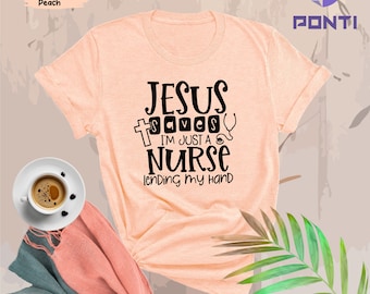 May include: A peach colored t-shirt with the text "Jesus Saves I'm Just A Nurse Lending My Hand" in black. The text is surrounded by a cross, a stethoscope, and a bandage.