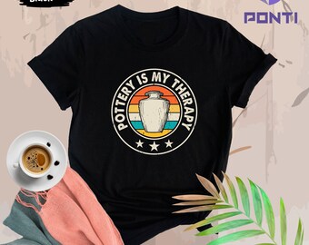 May include: Black t-shirt with a vintage-style graphic that says "Pottery is my therapy" with a stylized image of a ceramic vase.