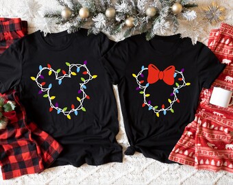 May include: Two black t-shirts with a Christmas light design in the shape of Mickey Mouse and Minnie Mouse. The Mickey Mouse shirt has a string of Christmas lights in the shape of his head. The Minnie Mouse shirt has a string of Christmas lights in the shape of her head with a red bow on top.