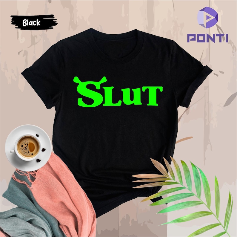 Op de afbeelding: Zwart T-shirt met een groene afbeelding met de tekst "SLUT" in een vetgedrukt lettertype.
