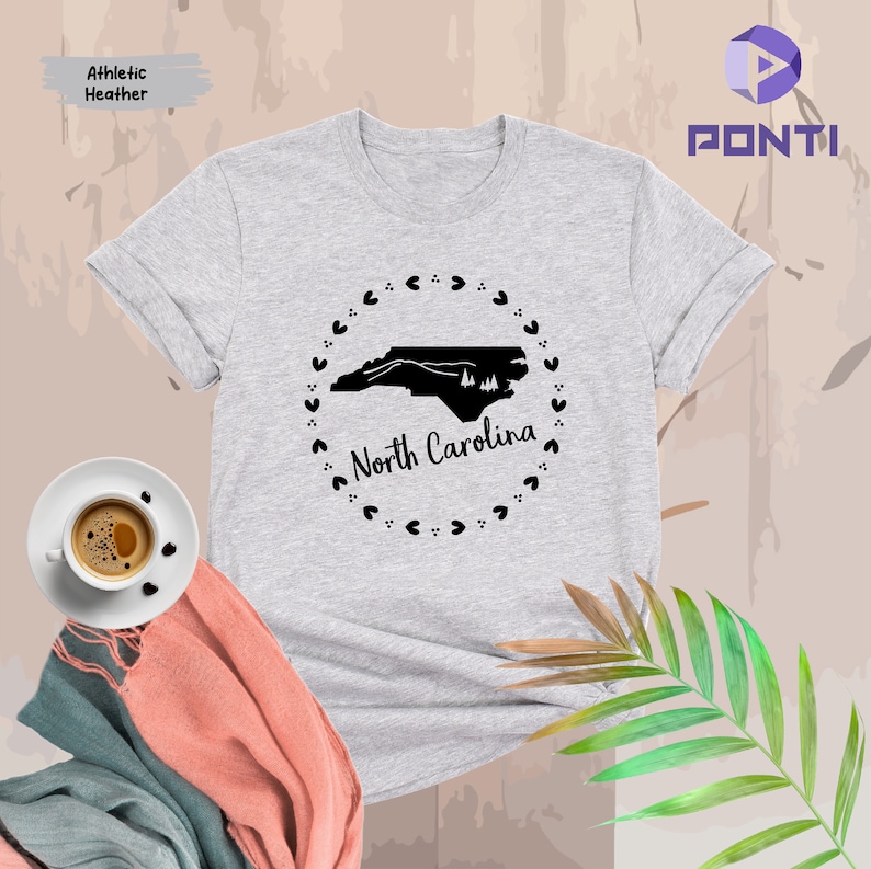 May include: A heather grey t-shirt with a black outline of the state of North Carolina and the words "North Carolina" in a circle of hearts.