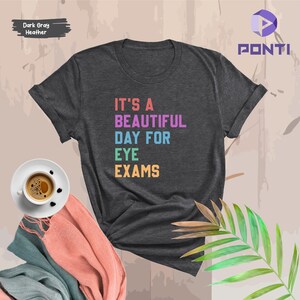 May include: Dark gray heather t-shirt with the text "It's a beautiful day for eye exams" in rainbow colors.