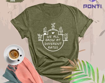 May include: A heather olive green t-shirt with a white graphic of potted plants and the text "We all grow at different rates".
