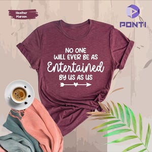 Könnte beinhalten: T-Shirt in Heidelbeer-Maroon mit dem Text "No one will ever be as entertained by us as us" in weißer Schrift mit einem weißen Pfeil und zwei Herzen.