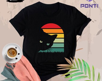 May include: Black t-shirt with a retro sunset design featuring a black cat peeking out from behind the sunset. The cat has green eyes.