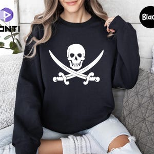 May include: Black crewneck sweatshirt featuring a white pirate flag design. The graphic includes a skull and crossbones with two crossed swords. The word "Black" is printed on a black circle in the upper right corner.