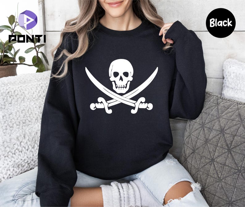 May include: Black crewneck sweatshirt featuring a white pirate flag design. The graphic includes a skull and crossbones with two crossed swords. The word "Black" is printed on a black circle in the upper right corner.
