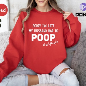May include: Red sweatshirt with the text "Sorry I'm late my husband had to poop #wifelife" in white.