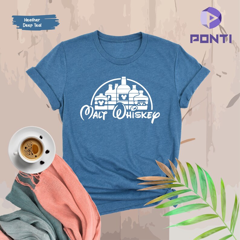 Op de afbeelding: Een blauw t-shirt met een witte afbeelding van een kasteel gemaakt van alcohol flessen met Mickey Mouse oren. De tekst "Malt Whiskey" staat onder het kasteel.