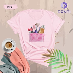 May include: Pink t-shirt with a watercolor illustration of a makeup bag with various makeup items, including lipstick, brushes, and foundation.