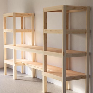 May include: Two wooden shelves with four shelves each, made of unfinished pine wood. The shelves are connected to each other and are freestanding.