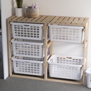 May include: A wooden shelf unit with four white plastic laundry baskets. The shelf unit has a natural wood finish and is made of slats. The baskets are rectangular and have a grid pattern.