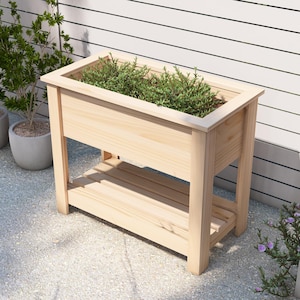 Könnte beinhalten: Ein natürlicher Holz-Pflanzkasten mit einem Regal, der auf einer Kiesfläche steht. Der Pflanzkasten ist leer und bereit für Pflanzen.